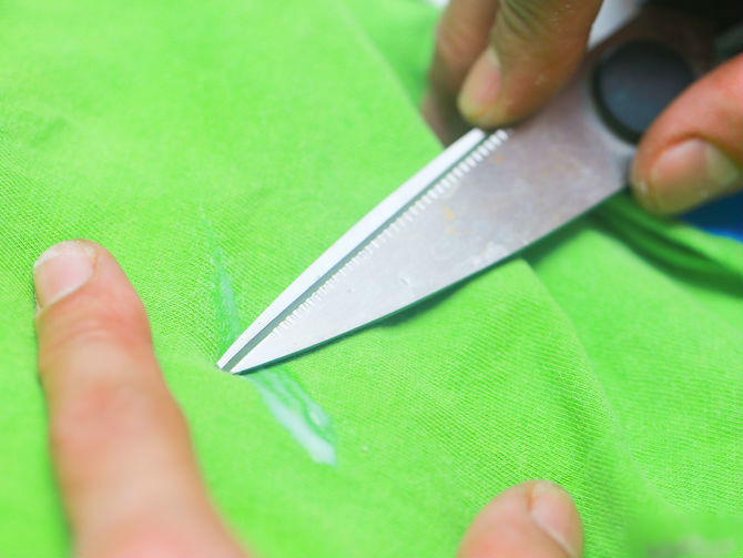 Ножницами убирают след с ткани